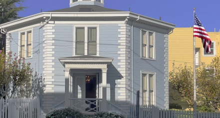 Image Of A Blue Octagonal Building With White Trim Next To A Flagpole With The American Flag On The Right.