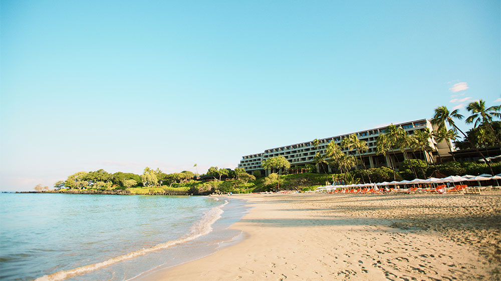 Beach and daytime exterior of the Mauna Kea Beach Hotel in Hawaii.